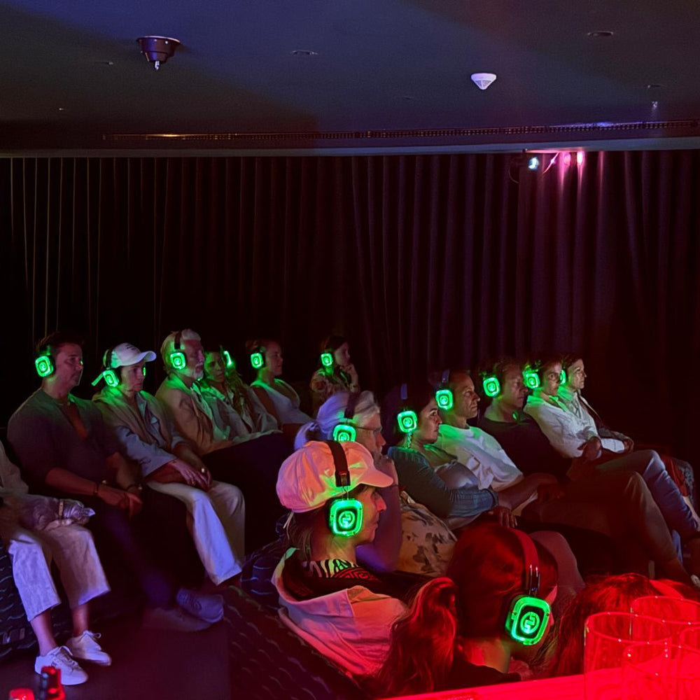 People wearing glowing green headphones in a dark room, possibly at a movie theater.