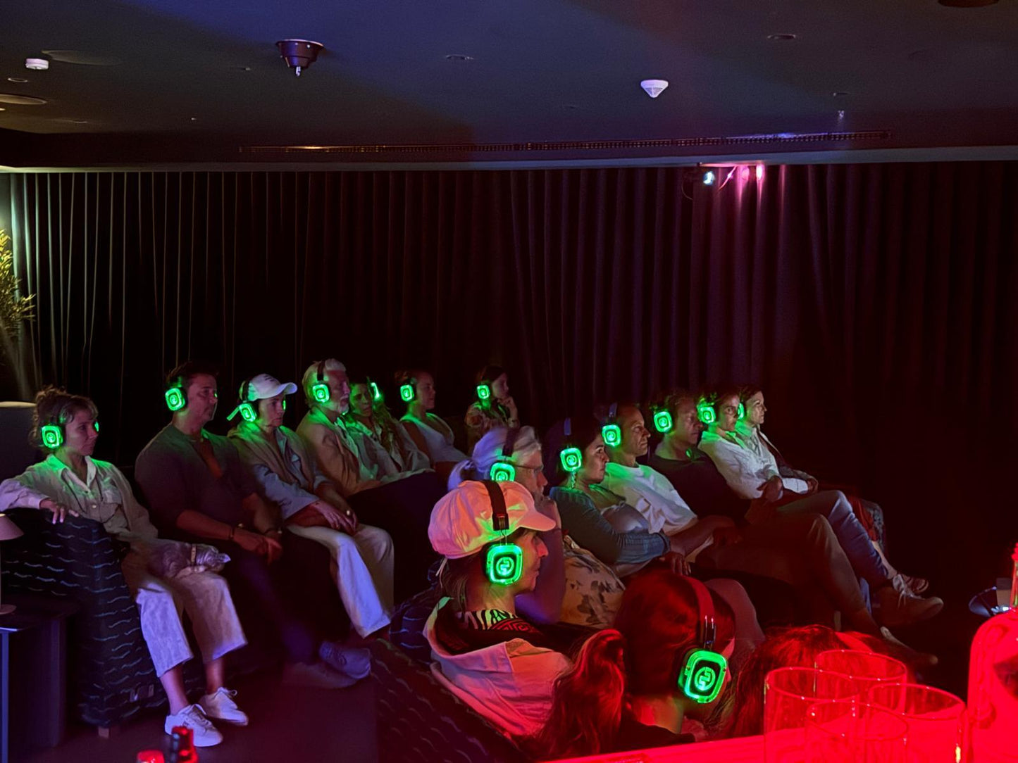 People wearing glowing green headphones in a dark room, possibly at a movie theater.