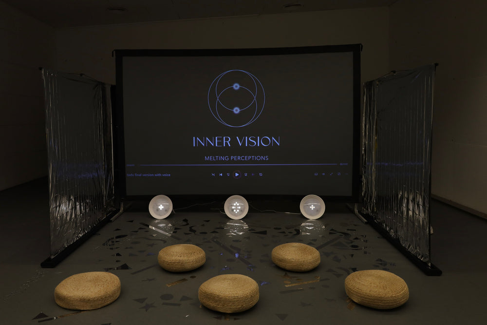 Dark room with a screen displaying 'INNER VISION' and various round objects on a table.