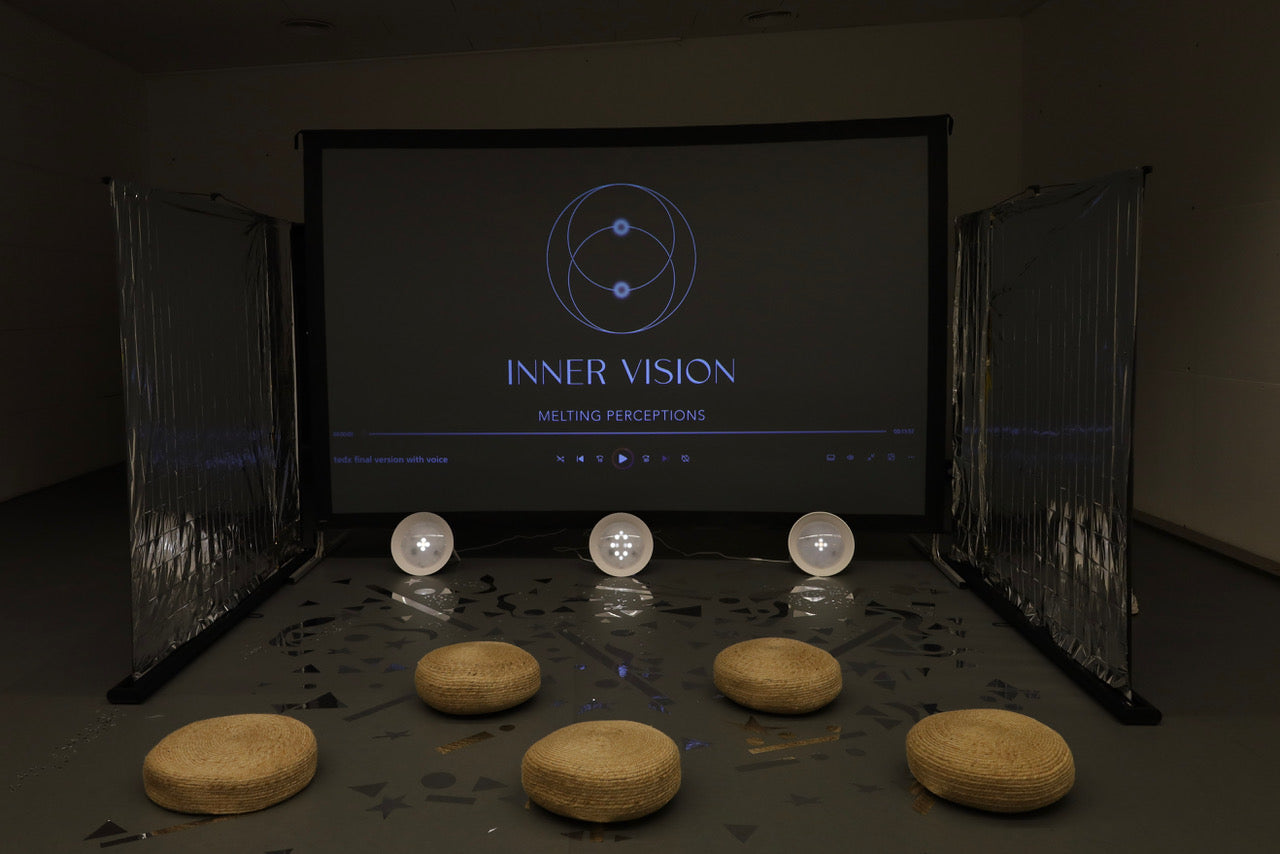 Dark room with a screen displaying 'INNER VISION' and various round objects on a table.