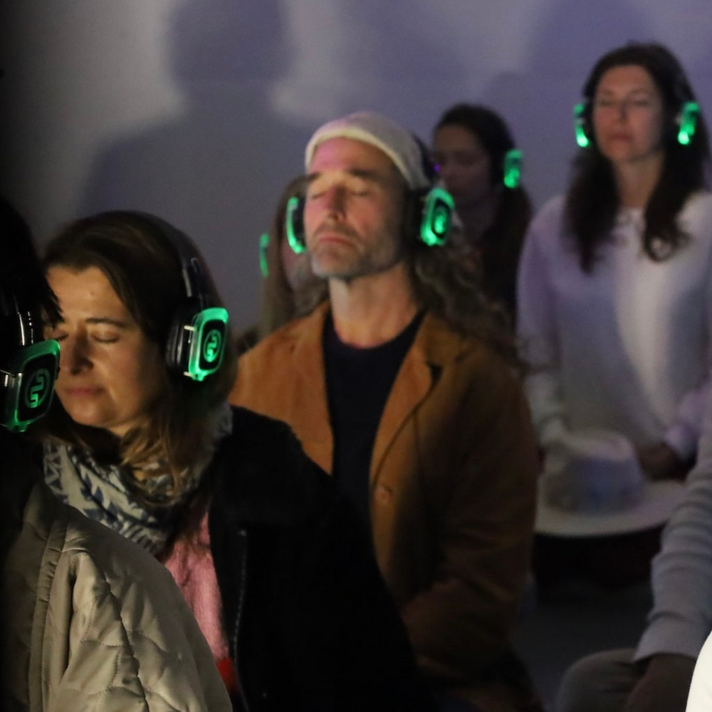 Group of people wearing headphones in a dimly lit room with a soft glow.
