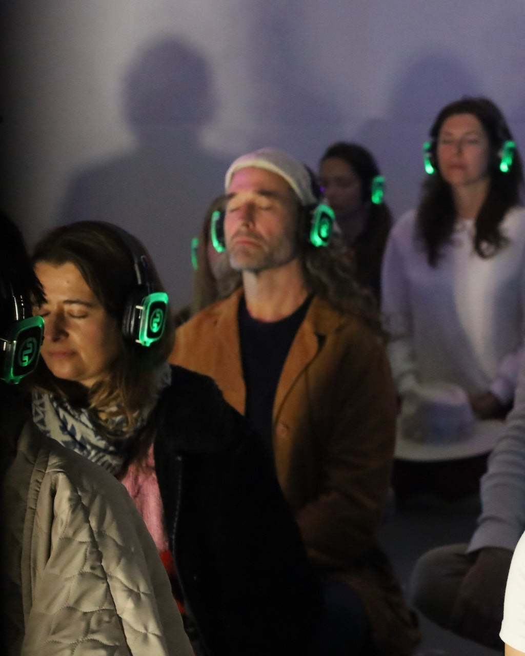 Group of people wearing headphones in a dimly lit room with a soft glow.