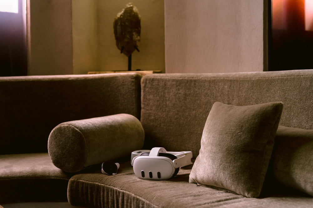 Gray sofa with a VR headset and controller on it, in a dimly lit room.